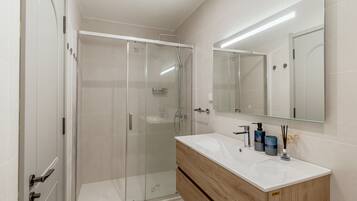 A modern bathroom with a glass-enclosed shower, a wooden vanity, and a large mirror.