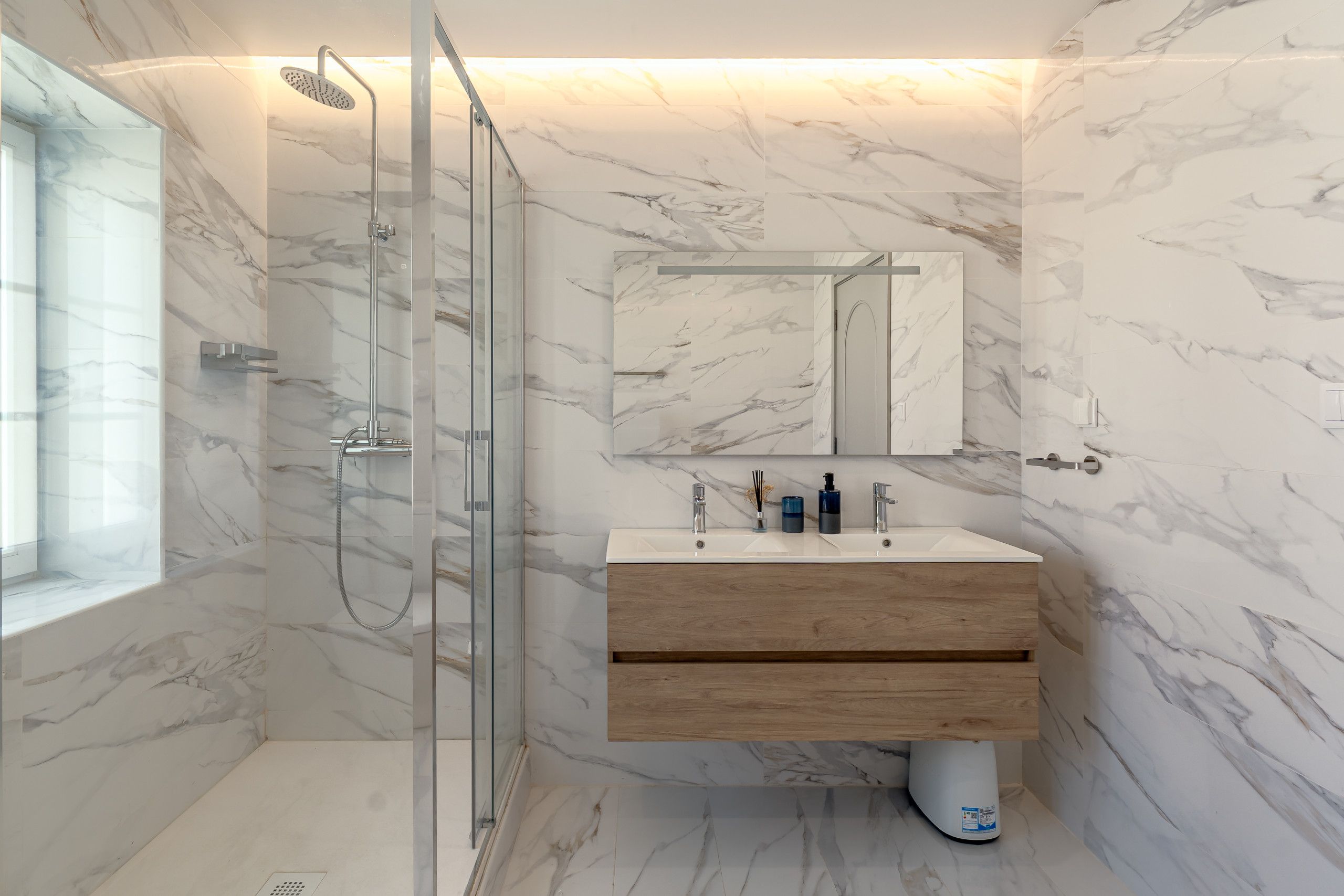A bathroom with a glass-enclosed shower, a wooden vanity, and a marble backsplash.