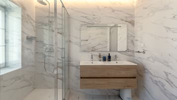 A bathroom with a glass-enclosed shower, a wooden vanity, and a marble backsplash.