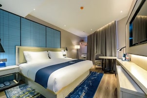 Una habitación de hotel con una cama grande, mesitas de noche, un escritorio, una silla, un televisor y una cortina.