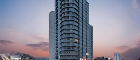 A high-rise building with a curved facade, multiple balconies, and a prominent entrance with signage.