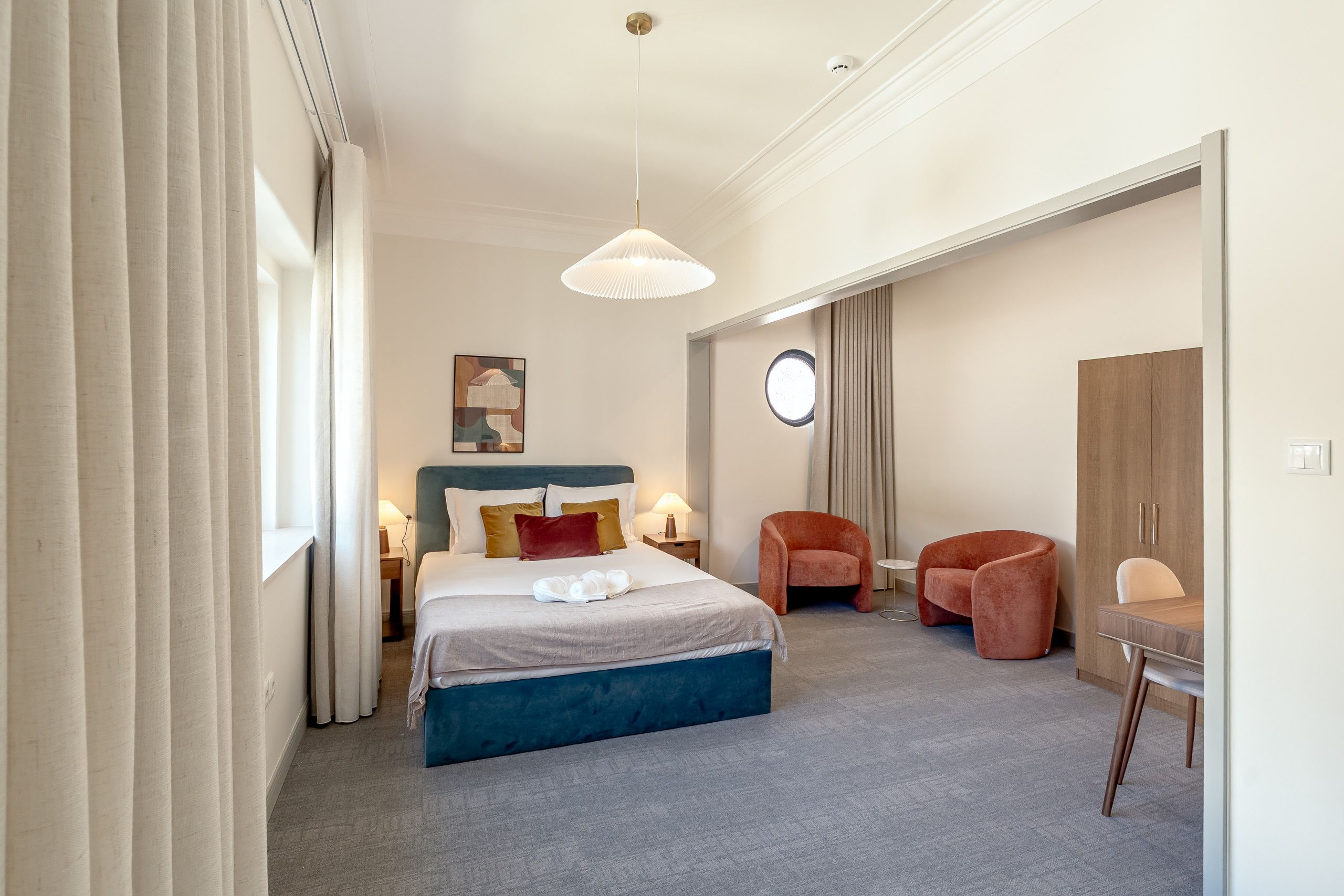 A hotel room with a bed, bedside tables, a desk, and chairs.