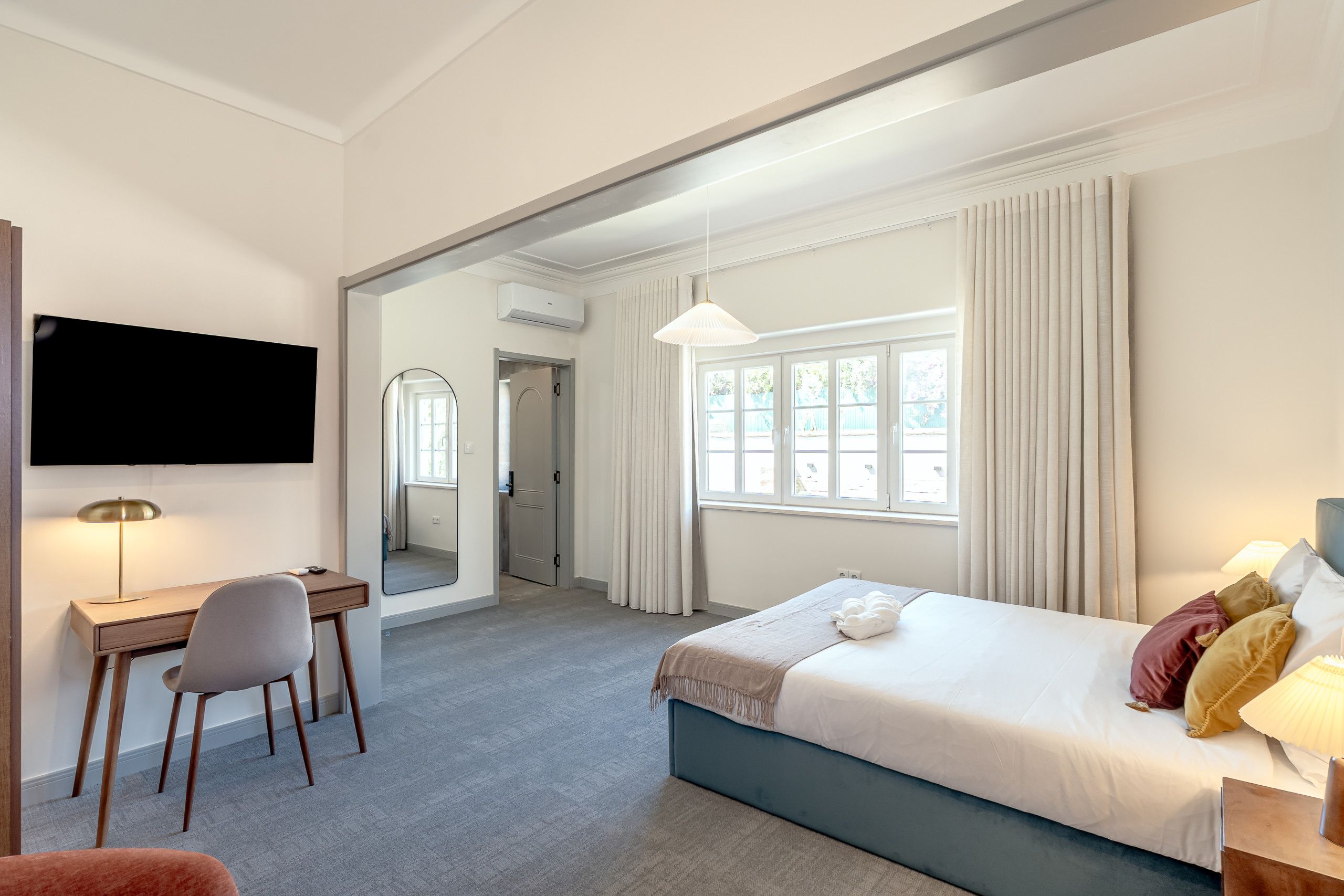 A hotel room with a bed, a desk, a chair, a television, and a window with curtains.