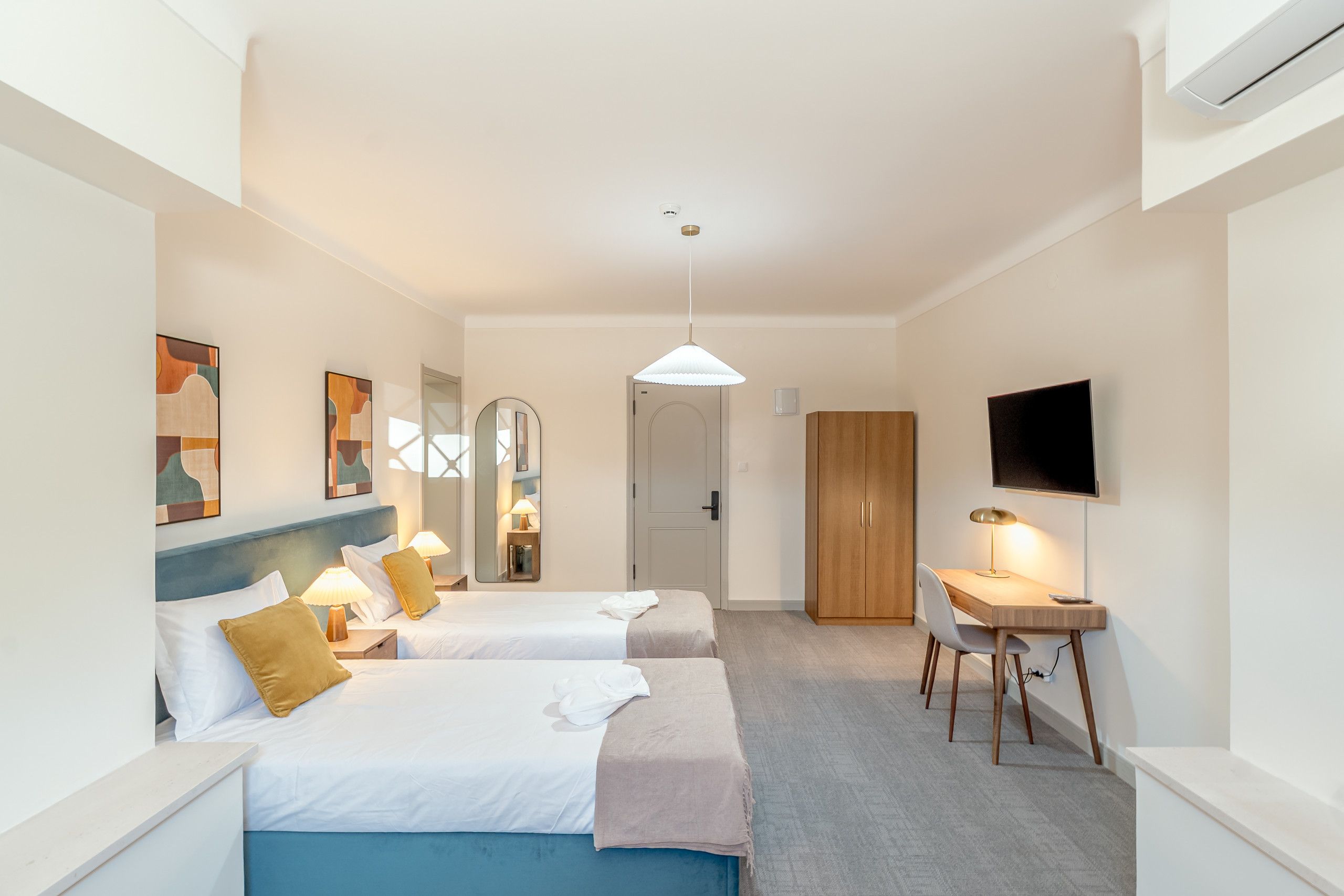 A hotel room with two beds, a desk, a TV, and a wardrobe.