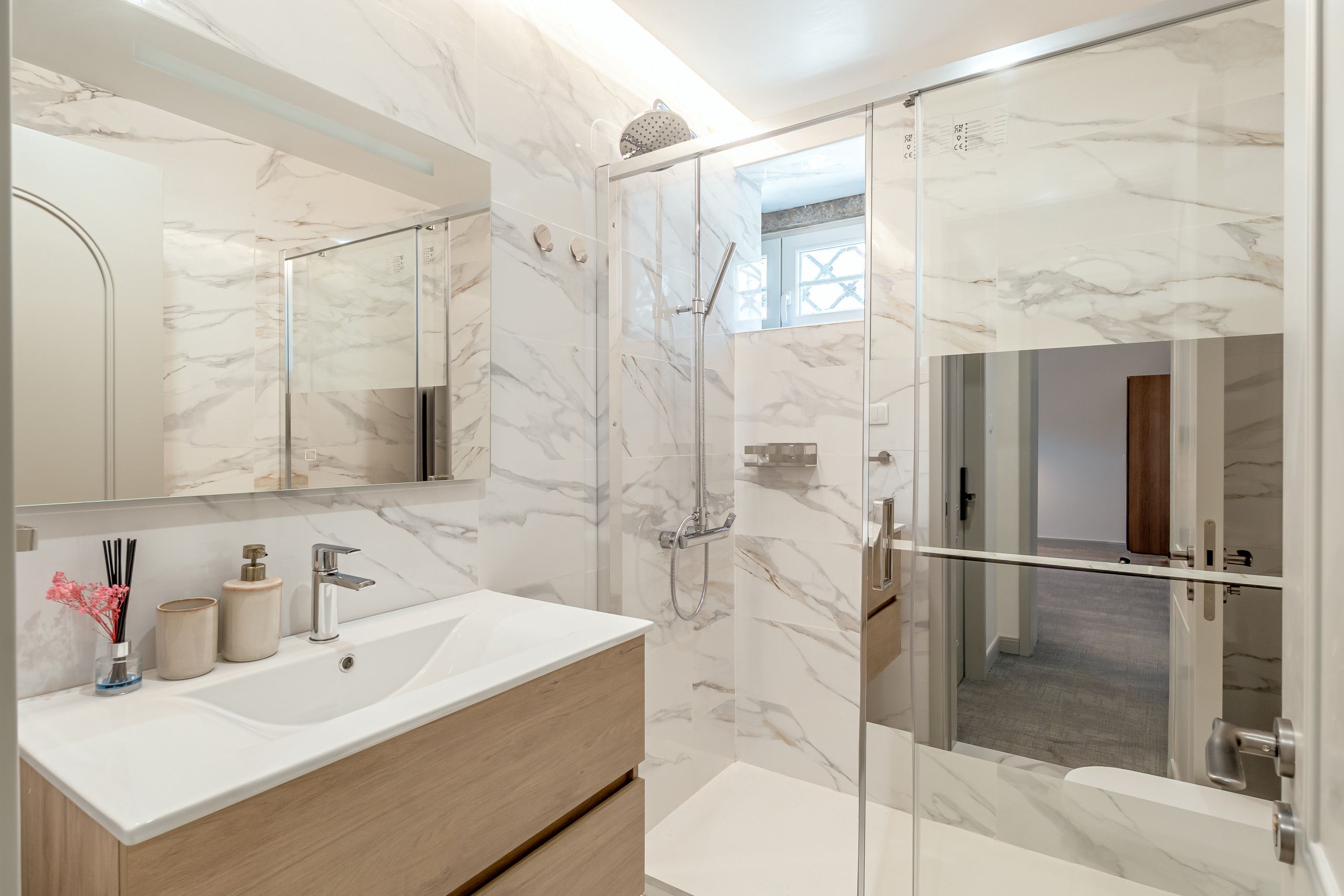 A modern bathroom with a marble wall, a glass-enclosed shower, and a wooden vanity.