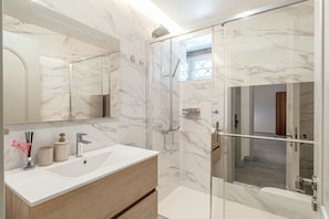 A modern bathroom with a marble wall, a glass-enclosed shower, and a wooden vanity. - Atlantic House 001 by Homing (Lisbon)