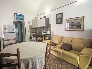 Ein kompakter Wohnbereich mit Esstisch, Sofa, Küchenzeile und einem gerahmten Bild an der Wand.