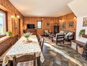 Um ambiente acolhedor com paredes de madeira, uma área de jantar com mesa e cadeiras, um sofá e uma televisão.