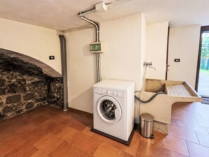 Ein Waschraum mit einer Waschmaschine, einem Waschbecken und einem Mülleimer.