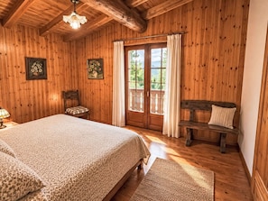 Ein Schlafzimmer mit Holzwänden, einem Bett, einer Bank, einem Stuhl und einem Fenster mit Vorhängen.