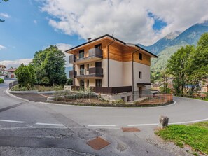 Ein modernes, zweistöckiges Gebäude mit Balkon, umgeben von Grünflächen und Bergen.