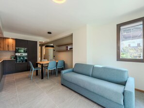 Ein modernes Wohnzimmer mit Sofa, Esstisch, Stühlen und einer Küchenzeile mit Herd.