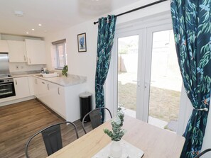 A modern kitchen with white cabinets, a built-in oven, and a dining area with a table and chairs. - 5 Warrington Lane (Coventry)