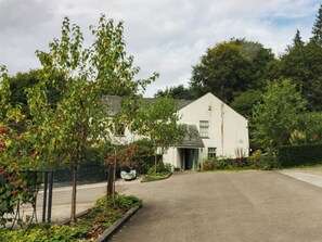 A two-story house with a paved driveway and a garden with various plants and trees. - Dunmail Raise, Grasmere Lodge (Ambleside)