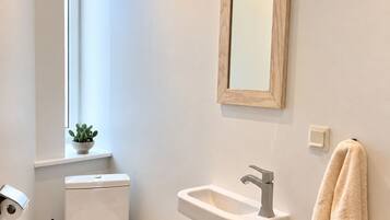 Casa de banho com sanita, lavatório, espelho e porta-toalhas.