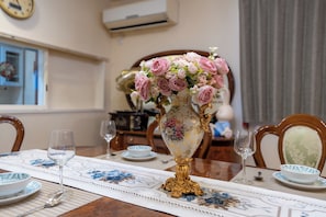 A dining table with a floral vase centerpiece, a clock on the wall, and a window with curtains. - Rabbit house (Edogawaku)