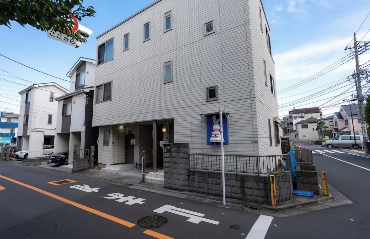A multi-story building with a gated entrance, a blue sign, and a street with marked lanes.