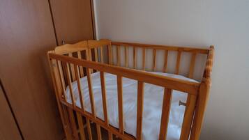 A wooden crib with a white mattress, positioned against a wall with a door and a small yellow object on the floor.