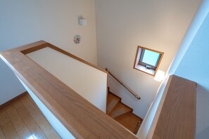 Een houten trap met een leuning, een klein raam aan de bovenkant en een wandlamp.