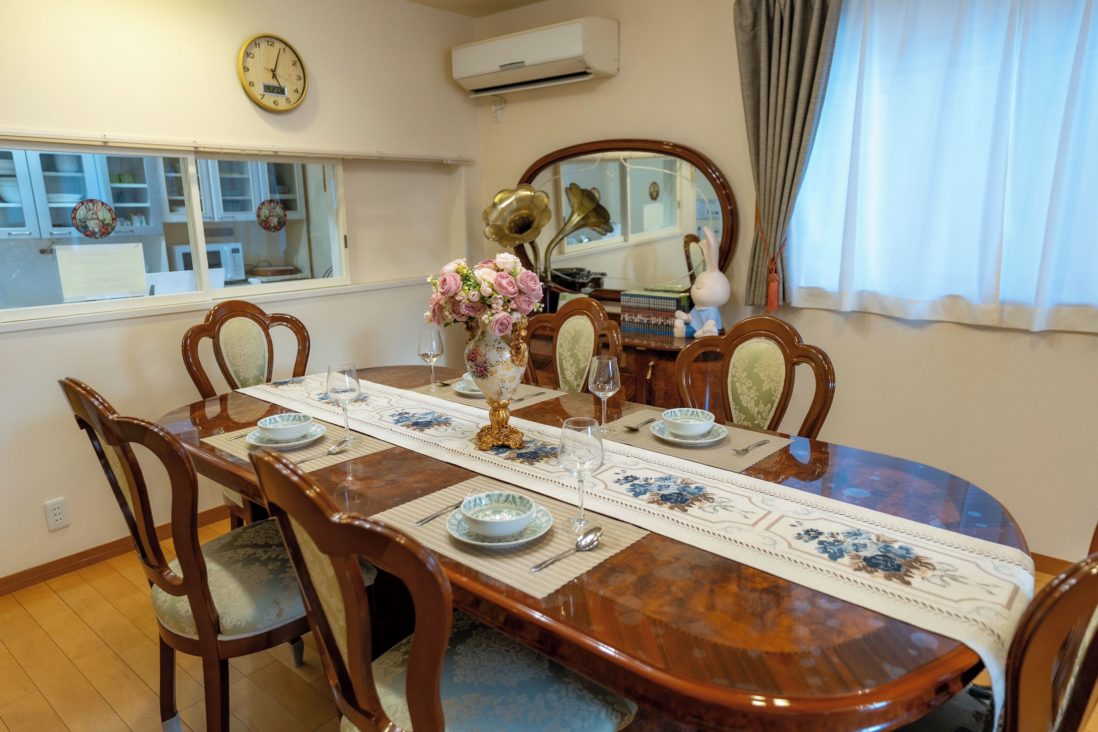 A dining room with a wooden table set for six, surrounded by chairs.