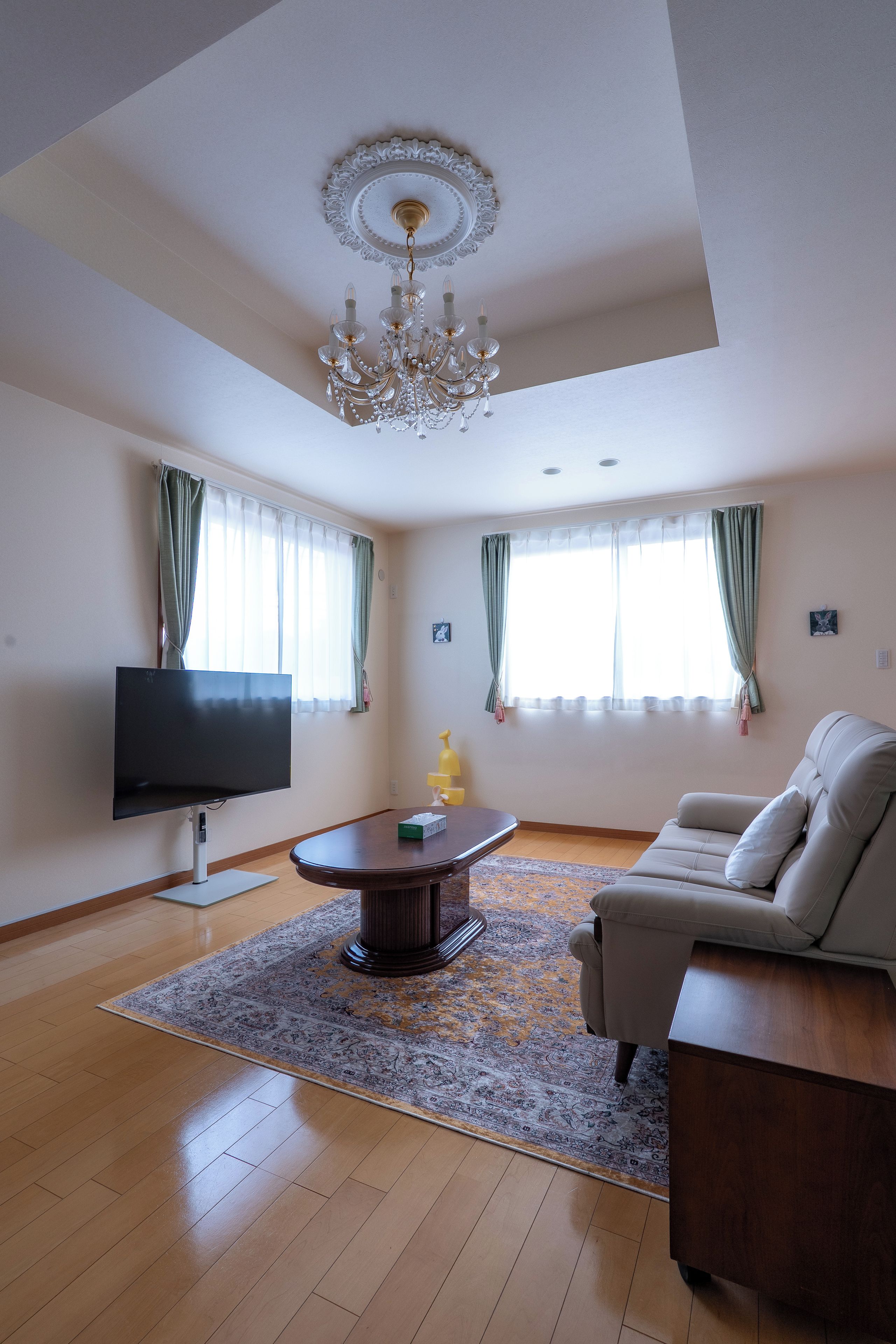 Uma sala de estar com televisão de tela plana, um sofá, uma mesa de centro e um lustre.