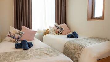A hotel room with two beds, a window, and a ceiling light.