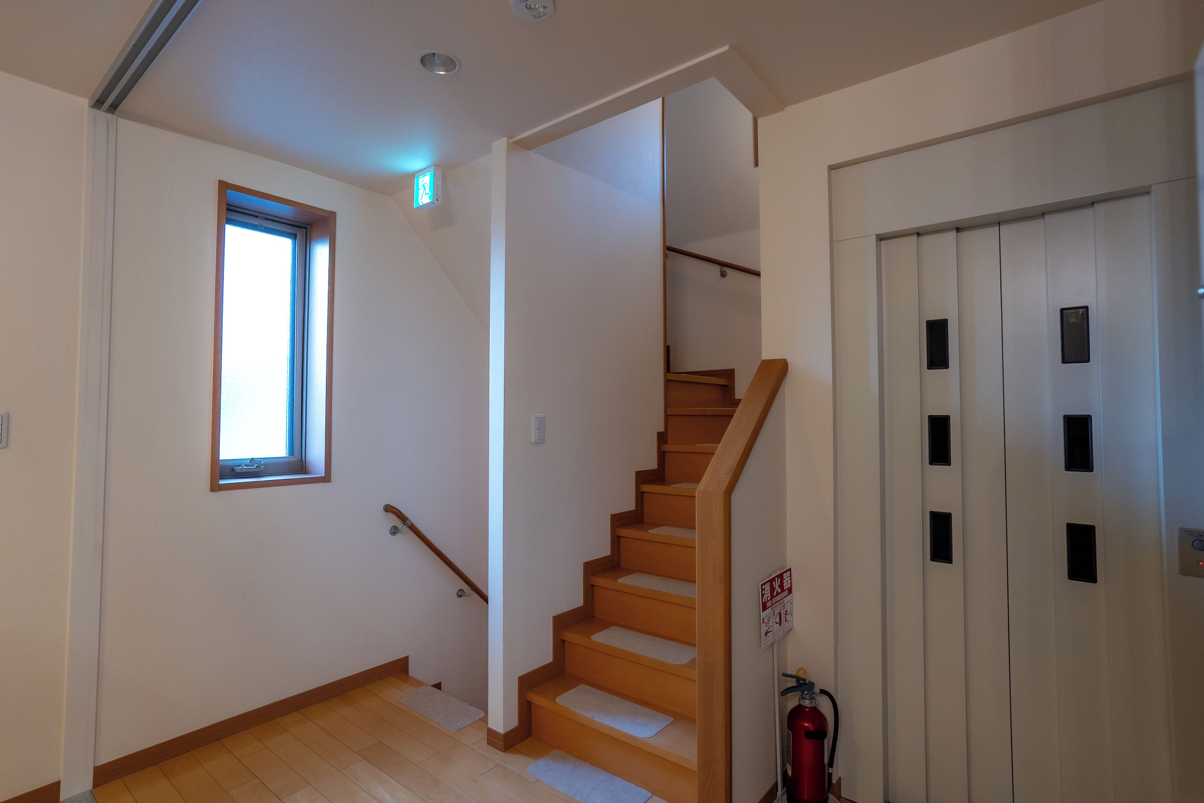 A staircase with wooden steps and a handrail, leading to a door with a fire extinguisher mounted on the wall.