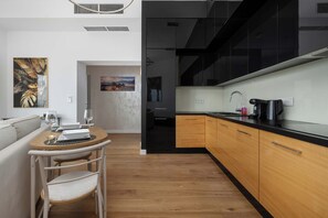 A modern kitchen with black cabinets, a wooden countertop, and a dining area with a table and chairs. - Wroclaw | Gwiaździsta 64 | Apartment with a View | Parking (Wrocław)