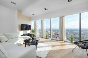 A modern living room with a large window, a sofa, a coffee table, and a TV mounted on the wall. - Wroclaw | Gwiaździsta 64 | Apartment with a View | Parking (Wrocław)