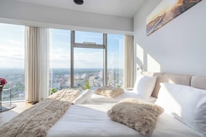 Ein modernes Schlafzimmer mit großem Fenster, einem Bett mit weichen Kissen und Blick auf die Stadt.