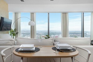 A modern dining area with a table set for two, overlooking a cityscape through large windows. - Wroclaw | Gwiaździsta 64 | Apartment with a View | Parking (Wrocław)