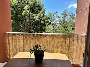 Ein Balkon mit einem Bambuszaun, einem Blumentopf und Blick auf Bäume und Gebäude.