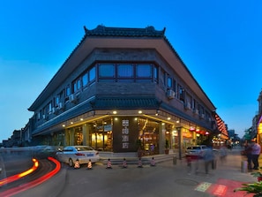A traditional building with a prominent entrance and multiple windows, located on a street with cars and traffic cones. - Choenix Hotel (Beijing)