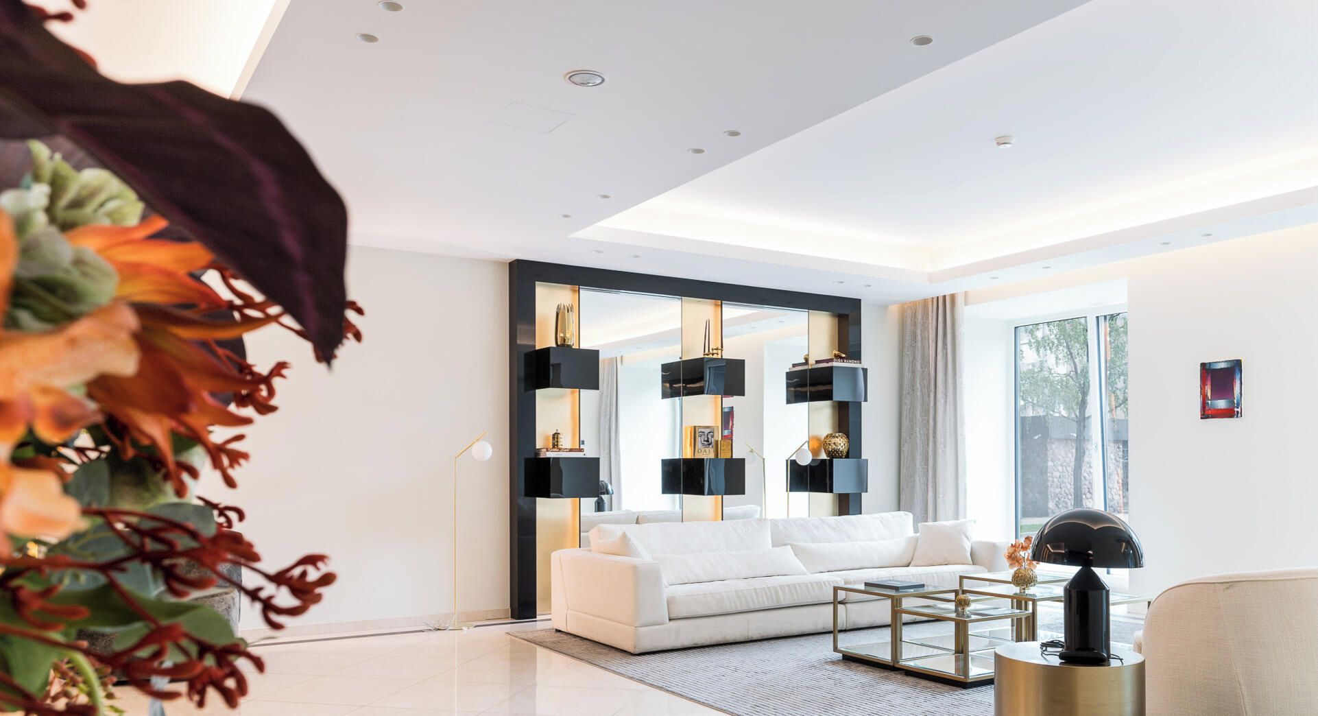 Ein modernes Wohnzimmer mit einem weißen Sofa, einem Glastisch und einer Zimmerpflanze.