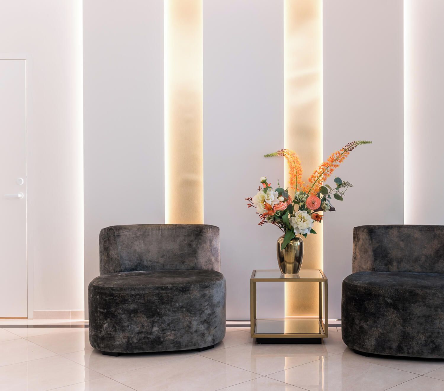 Un intérieur moderne avec deux canapés aux couleurs sombres, une table d’appoint au plateau en verre et un vase rempli de fleurs.