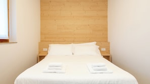 Ein ordentlich bezogenes Bett mit weißen Leinen und Handtüchern, ein hölzerner Kopfteil und ein kleiner Nachttisch mit Steckdose.