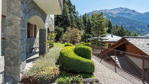 A stone building with a stone staircase, a wooden bench, and a fenced garden with neatly trimmed bushes and flowers. - Sertorelli 45 (Bormio)