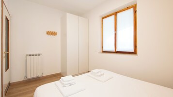 Una camera d'albergo con un letto, un termosifone, un armadio e una finestra con tende.
