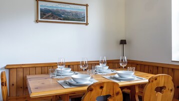 Un tavolo da pranzo apparecchiato con piatti bianchi, ciotole e bicchieri da vino, circondato da una panca e sedie in legno.