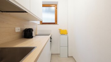 Una cucina compatta con piano di lavoro in legno, lavello incassato, una piccola finestra e un elettrodomestico giallo su un mobile bianco.