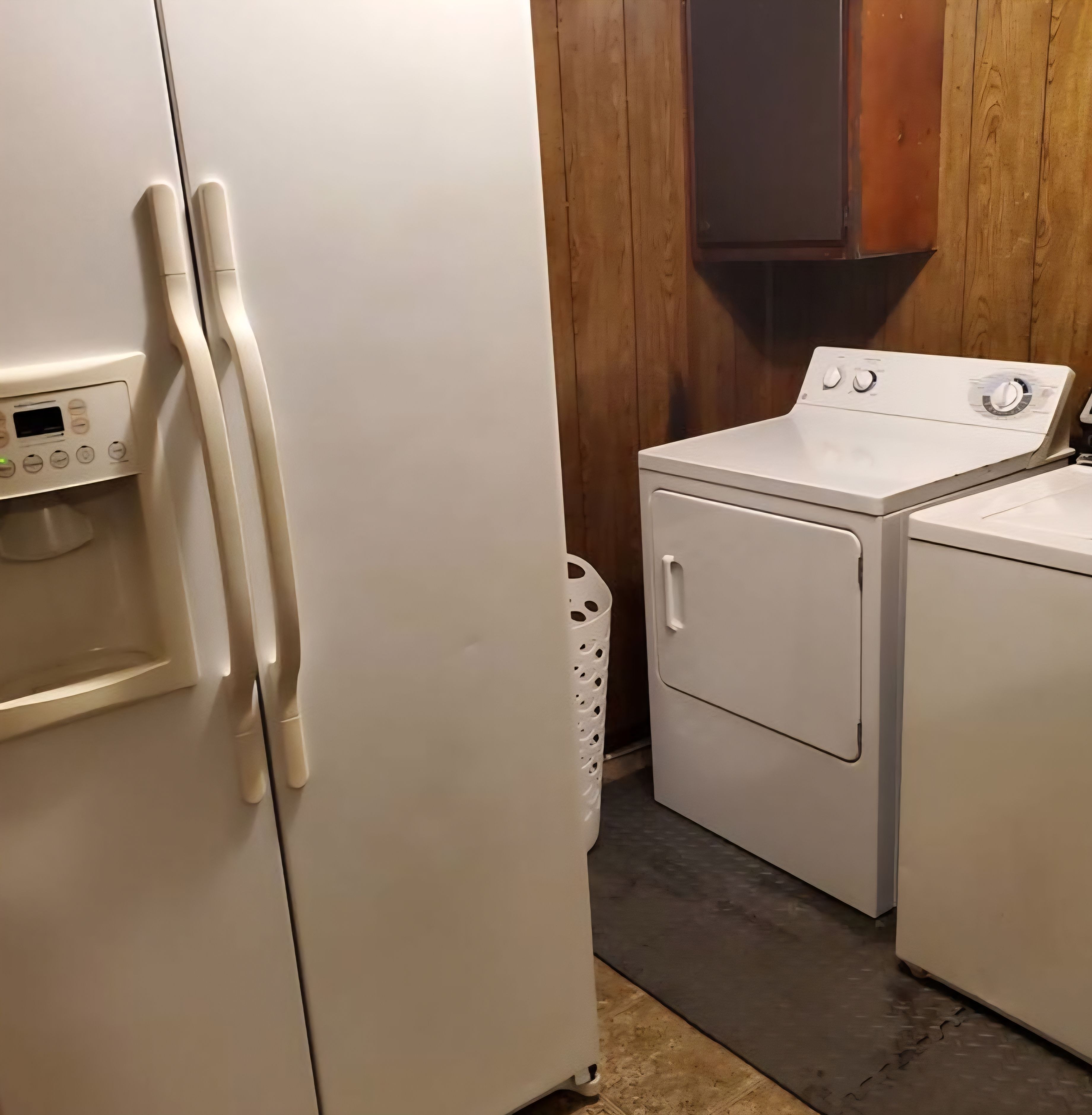 A laundry area with a front-loading washer and dryer, a control panel, and a wooden wall.