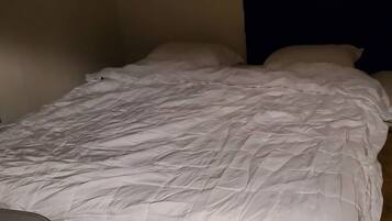 A single bed with a white duvet in a room with a dark wall and a wooden floor.