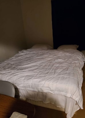 Una cama individual con edredón blanco en una habitación con pared oscura y suelo de madera.