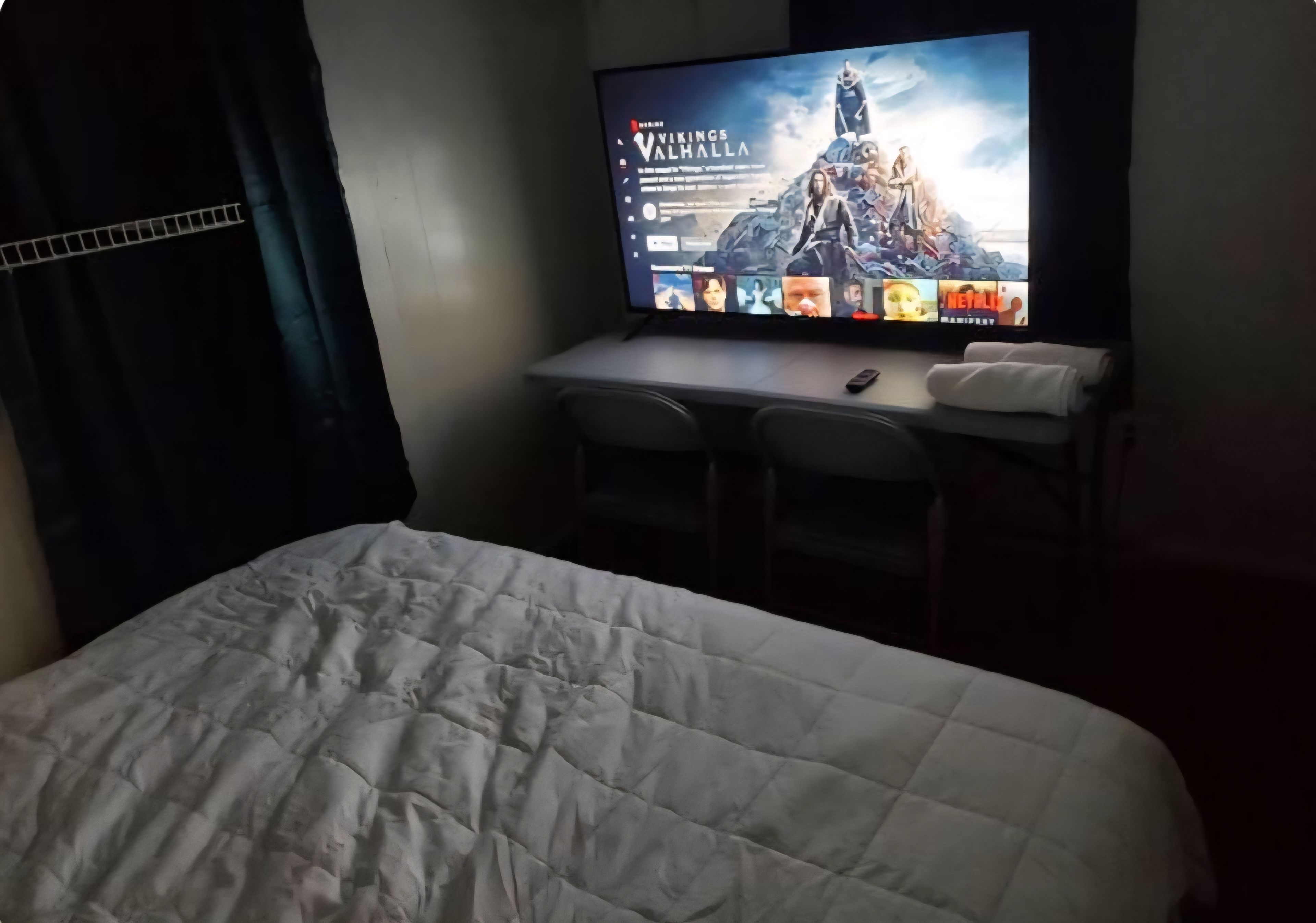 A hotel room with a bed, a desk with a computer, and a TV displaying a movie poster.
