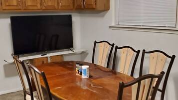 A dining area with a wooden table, six chairs, a television, and wooden cabinets.