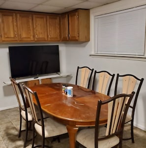Un comedor con una mesa de madera, seis sillas, un televisor y armarios de madera.