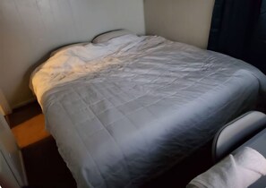 A bed with a grey quilt, a pillow, and a headboard.