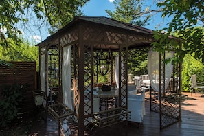 A wooden gazebo with a lattice roof, surrounded by a wooden deck and outdoor furniture. - Anerada Inn Suites Pool & Spa | Lilac Suite (Megalo chorio)
