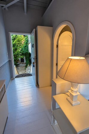 Ein Flur mit einer weißen Tür, die zu einem Garten führt, einer Lampe auf einem Tisch und einer weißen Bank.