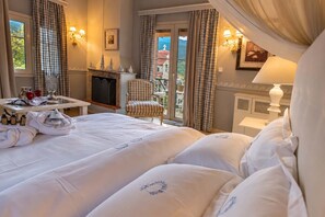 A hotel room with a bed, a chair, a fireplace, and a view of a building through the window. - Anerada Inn Suites Pool & Spa | Blue Suite (Megalo chorio)